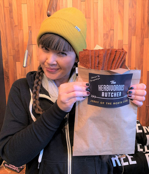 a woman holding up a brown paper envelope with vegan jerky sticking out the top