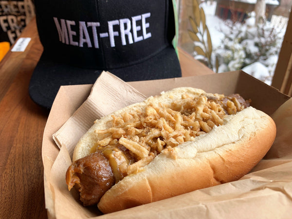 A vegan bacon brat topped with mustard and fried onions