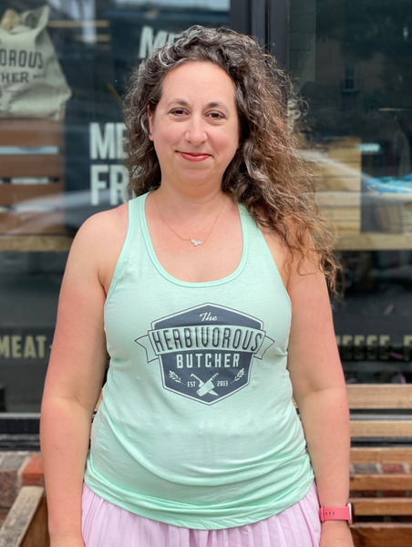 person wearing a light mint green tank top with The Herbivorous Butcher logo on it