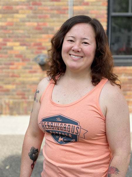 person wearing a light peach tank top with The Herbivorous Butcher logo on it
