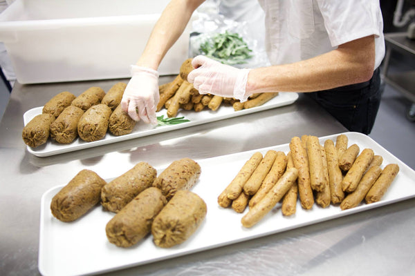 a person placing logs of vegan meat on white trays
