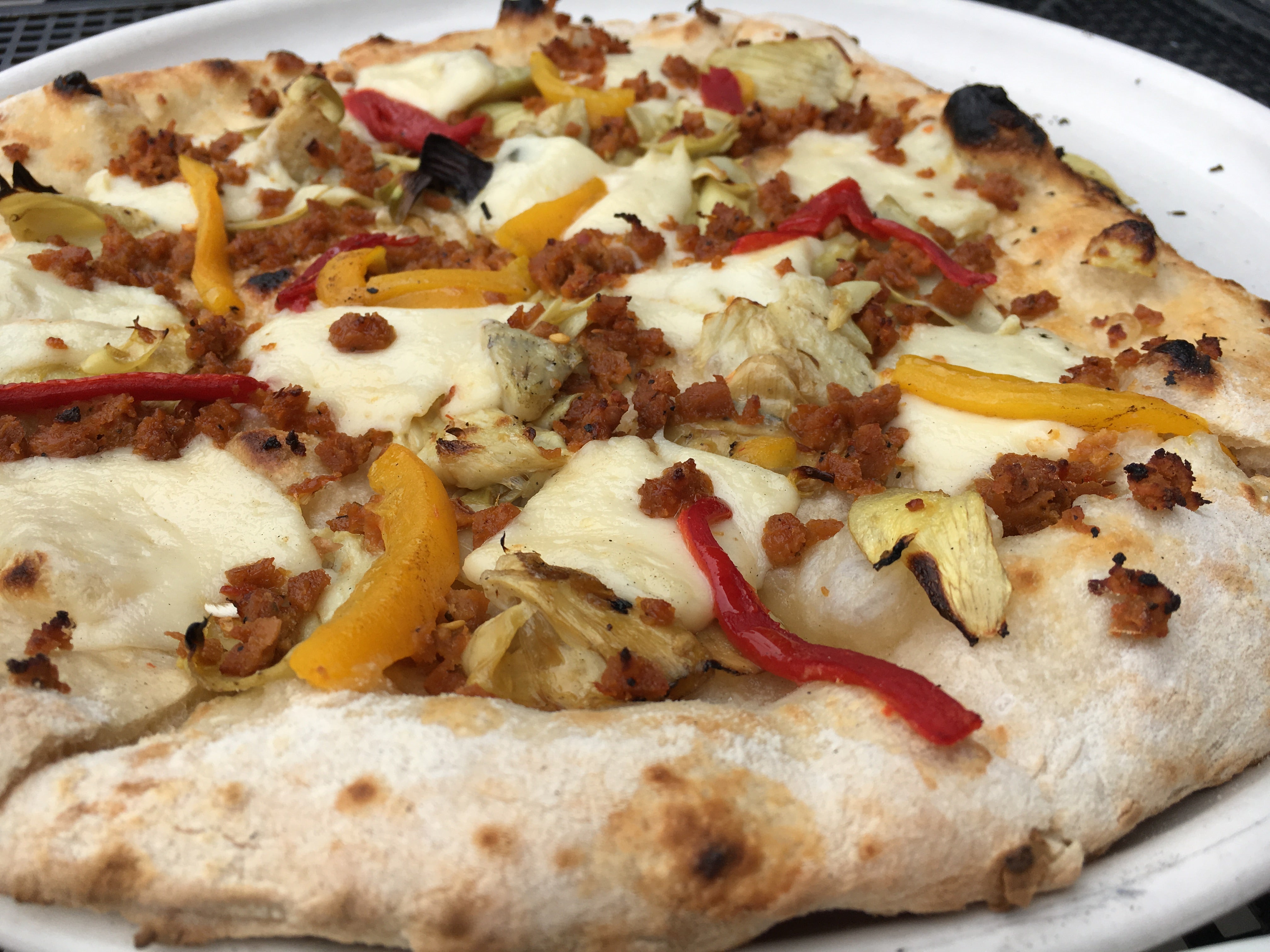 vegan pizza topped with mozzarella, sliced peppers, and sausage crumbles