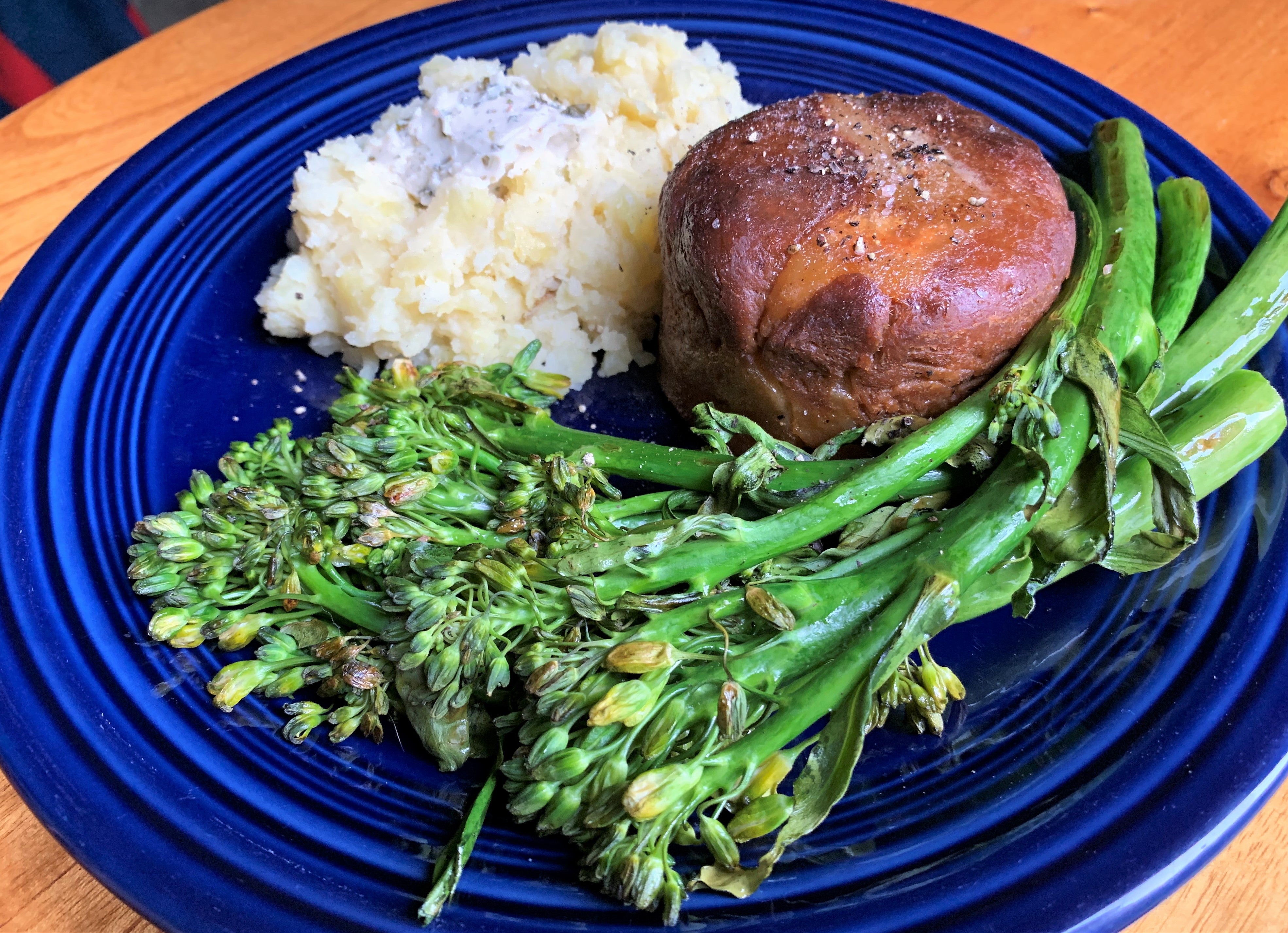 a blue plate topped with round vegan filet mignon and sides of broccolini and mashed potatoes